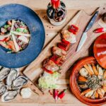 Top view of French gourmet dishes including seafood salad, grilled skewers, oysters, and wine in Angers, France.